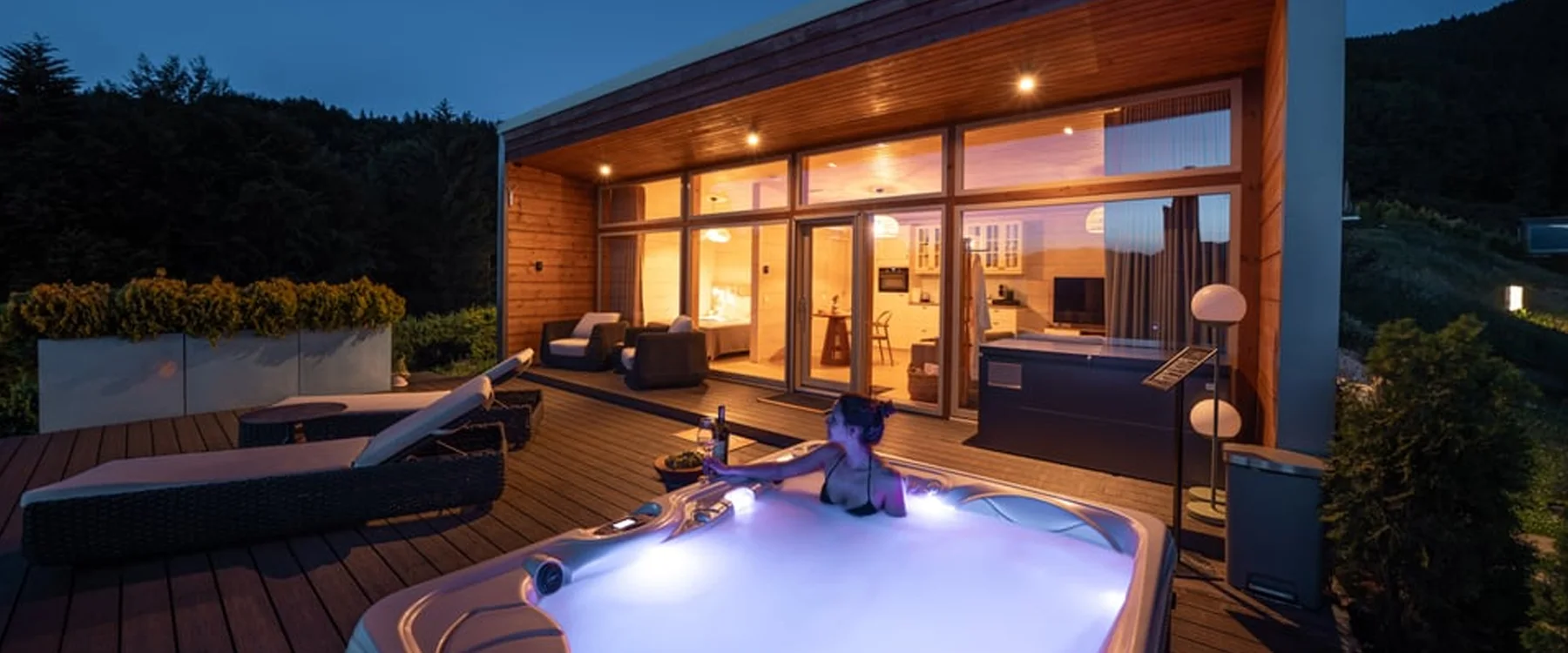Eden Hill villa illuminated at night, with a woman in the hot tub on its wooden terrace.