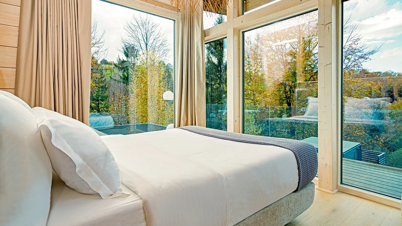 Eden Hill bedroom with white bedding and floor-to-ceiling windows overlooking autumn trees.