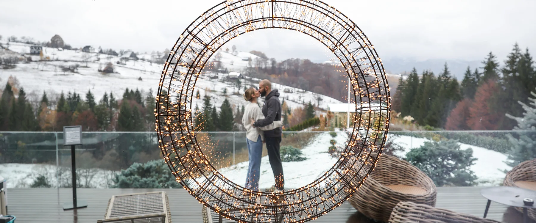 Couple embracing beneath a decorated circular arch on a snowy Eden Hill terrace.
