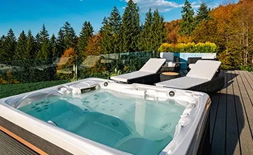 Hot tub and two loungers on an Eden Hill wooden terrace beside autumn trees.