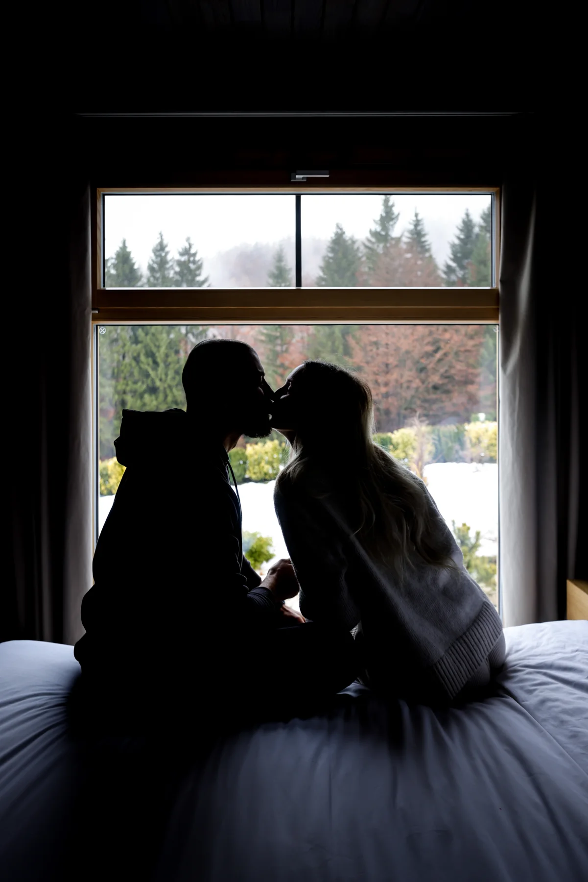 Silhouettes of a couple sitting on a bed in front of a window.