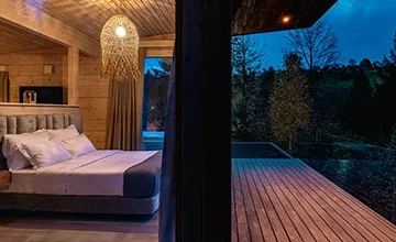 Wood-lined Eden Hill bedroom seen through an open glass door leading onto the terrace at dusk.
