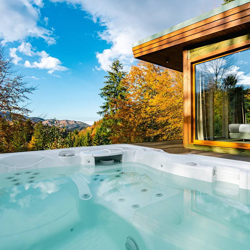 Jacuzzi exterior lângă o vilă din lemn Eden Hill, cu un copac portocaliu și cer albastru.
