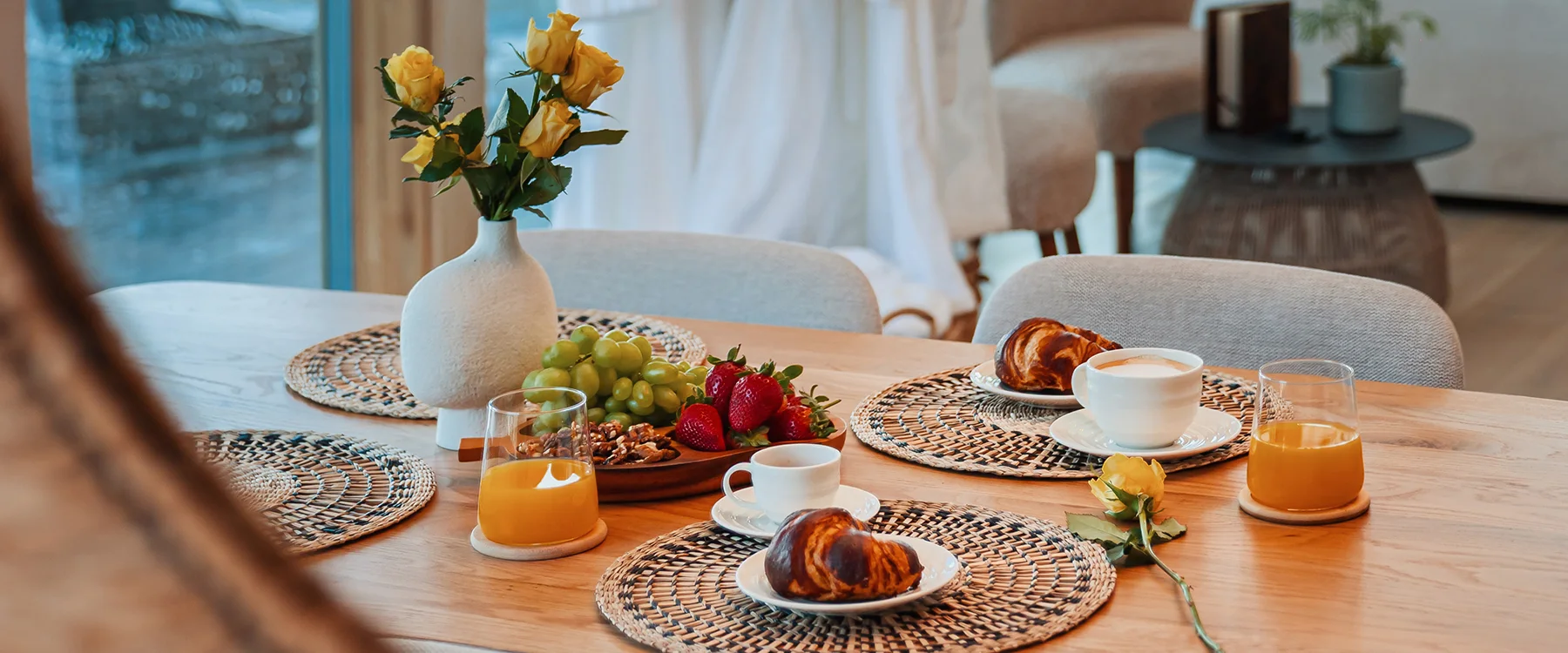 Breakfast table with croissants, fruit, coffee, orange juice and yellow roses.