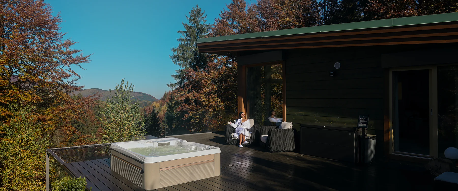 Eden Hill terrace with a hot tub and a woman seated in the villa's shade beside orange autumn trees.