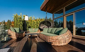 Wicker sofas with green cushions and a hanging chair on an Eden Hill wooden terrace.