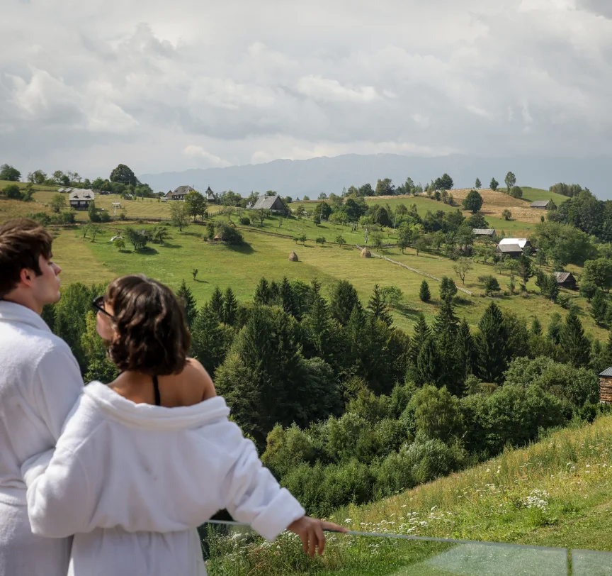 Cuplu în halate albe privind valea verde de la balustrada terasei Eden Hill.