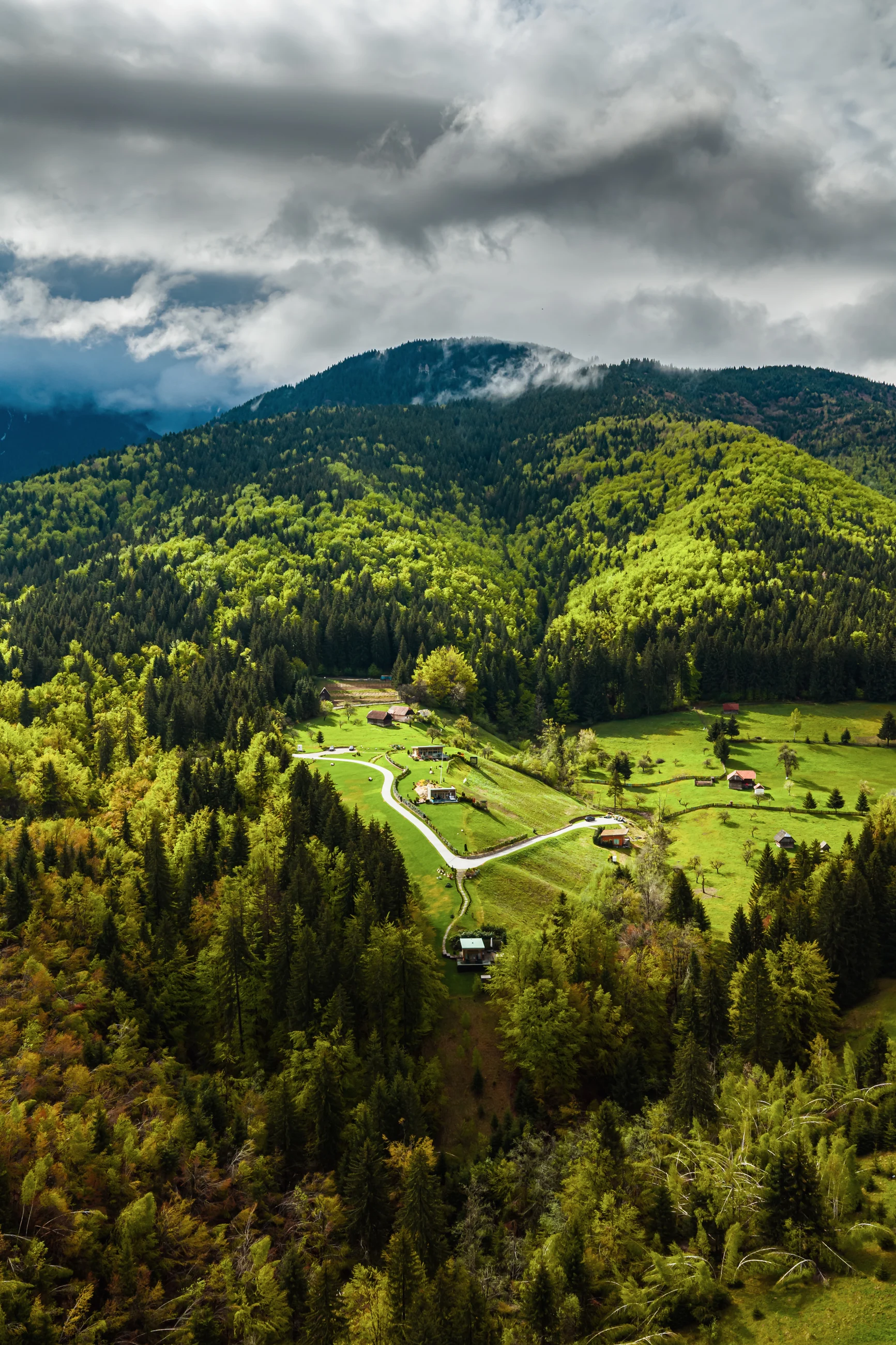 Eden Hill villas in a green valley surrounded by forest, seen from the air beneath low clouds.